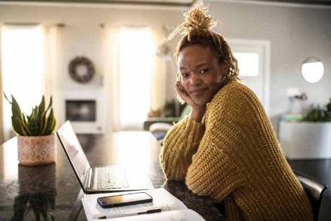 Woman in a yellow knitted jumper working at a laptop at a kitchen counter