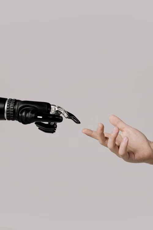 A black robotic hand and a human hand reaching towards each other, fingertips almost touching